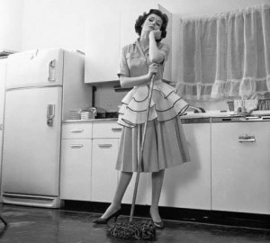 1950s Bored Woman Housewife Wearing Apron Leaning On Mop On Kitchen Floor